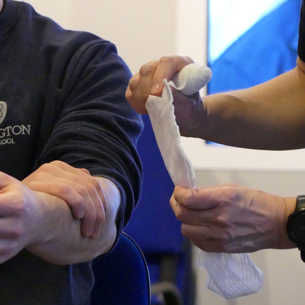 Trainer holding a wound pad up to a bleeding arm